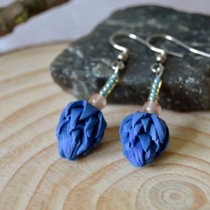 May include: A pair of blue flower earrings with silver hooks and beads. The earrings are made of polymer clay and have a delicate, feminine look.