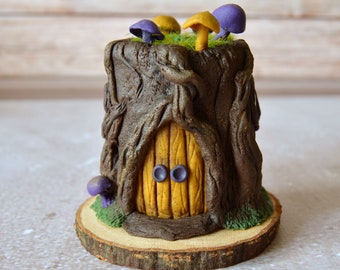 May include: A brown tree stump sculpture featuring a yellow wooden door with two purple circular knobs. The top is covered in green moss with several small purple and yellow mushrooms. The entire structure sits on a round wooden slice base.