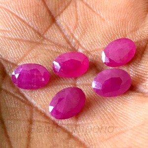 May include: Six oval-shaped, pink gemstones with a faceted cut. The gemstones are arranged in a semi-circle on a hand.