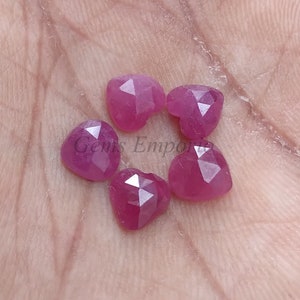 Puede incluir: Seis gemas facetadas en forma de corazón, de un tono rosa vibrante. Las gemas se muestran sobre una superficie clara, mostrando sus superficies pulidas y formas únicas. Las gemas probablemente se utilizan para la fabricación de joyas.