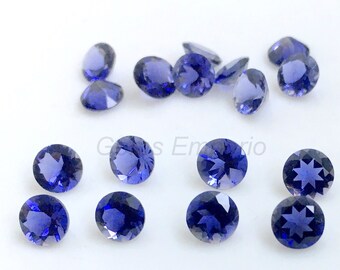 May include: A collection of round, faceted, deep blue gemstones. The gems are scattered on a white surface, showcasing their brilliant cut and color. The gems are of varying sizes and shapes.