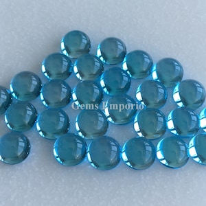 May include: A group of 20 round, light blue cabochon gemstones. The gemstones are smooth and shiny, and they are arranged in a loose pile.