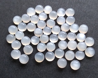 May include: A pile of white moonstone cabochons, each with a smooth, rounded surface and a subtle iridescent sheen.