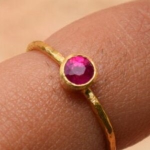 Pu&ograve; includere: Un delicato anello d'oro con una singola pietra preziosa rotonda di colore rosa brillante.