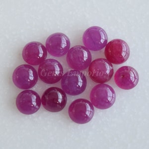 Op de afbeelding: Een groep van 14 ronde, roze robijn cabochons. De cabochons zijn glad en gepolijst, met een lichte glans.