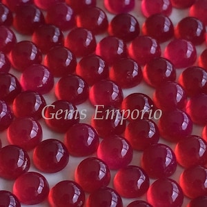 May include: A collection of 50 round, red cabochon gemstones. The gemstones are smooth and polished, with a glossy finish.