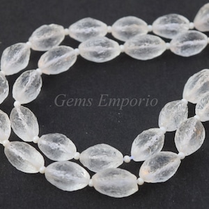 May include: A strand of clear quartz crystal beads, each bead is faceted and oval shaped. The beads are strung on a white thread and are arranged in a double strand.