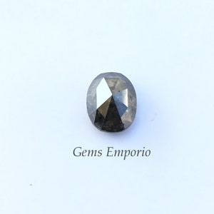 Puede incluir: Una piedra preciosa negra de forma ovalada con un corte facetado. La piedra preciosa est&aacute; sobre un fondo blanco con el texto "Gems Emporio" debajo.