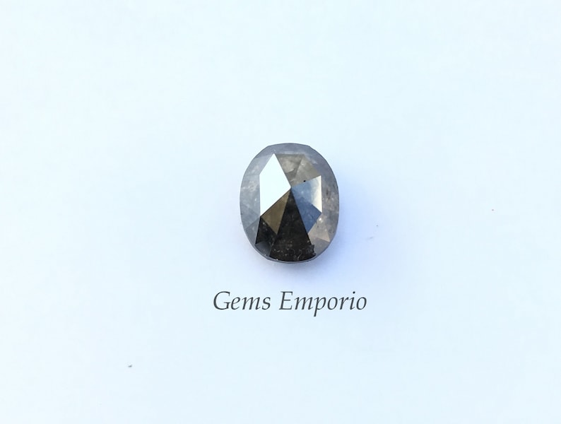 Puede incluir: Una piedra preciosa negra de forma ovalada con un corte facetado. La piedra preciosa est&aacute; sobre un fondo blanco con el texto "Gems Emporio" debajo.