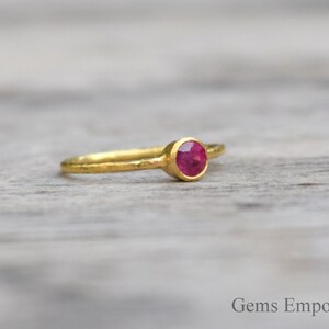 Pu&ograve; includere: Un delicato anello d'oro con una singola pietra preziosa rotonda di colore rosso incastonata al centro.