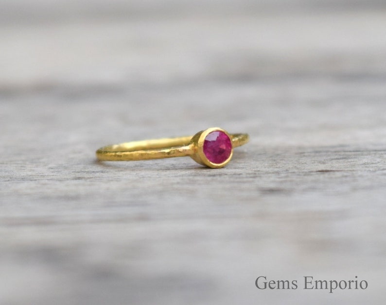 Pu&ograve; includere: Un delicato anello d'oro con una singola pietra preziosa rotonda di colore rosso incastonata al centro.