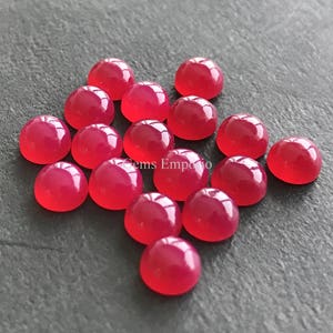 Könnte beinhalten: Eine Gruppe von 15 runden, rosafarbenen Cabochon-Edelsteinen. Die Edelsteine sind glatt und poliert und liegen lose in einem Haufen.