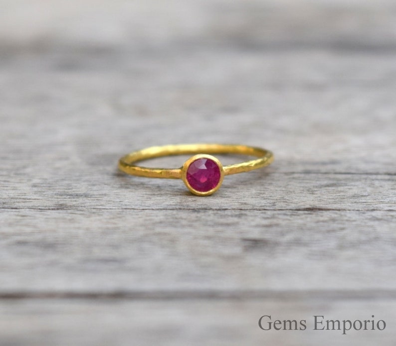 Pu&ograve; includere: Un delicato anello d'oro con una piccola pietra preziosa rotonda di colore rosso rubino incastonata al centro. La fascia &egrave; testurizzata e ha una finitura martellata.