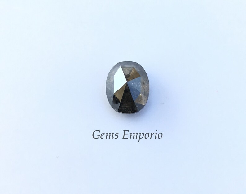 Puede incluir: Una piedra preciosa negra de forma ovalada con un corte facetado. La piedra preciosa est&aacute; colocada sobre un fondo blanco.