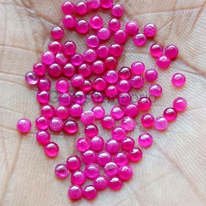 Puede incluir: Una colección de piedras preciosas de rubí redondas, de color rosa brillante. Las piedras preciosas son lisas y pulidas, y están esparcidas sobre una superficie de color claro.