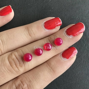 May include: Four round, pink cabochon gemstones, approximately 6mm in diameter, are displayed on a hand. The gemstones are smooth and polished. The text "Gems Emporio" is visible in the image.