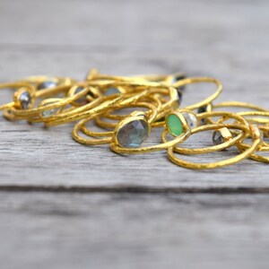 Pu&ograve; includere: Una collezione di anelli d'oro con varie pietre preziose colorate, tra cui verde, blu e grigio. Gli anelli sono impilati uno sopra l'altro su una superficie di legno.