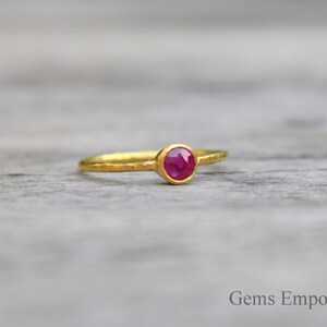 Pu&ograve; includere: Un anello d'oro con una pietra preziosa di rubino rosso. L'anello ha una texture martellata.