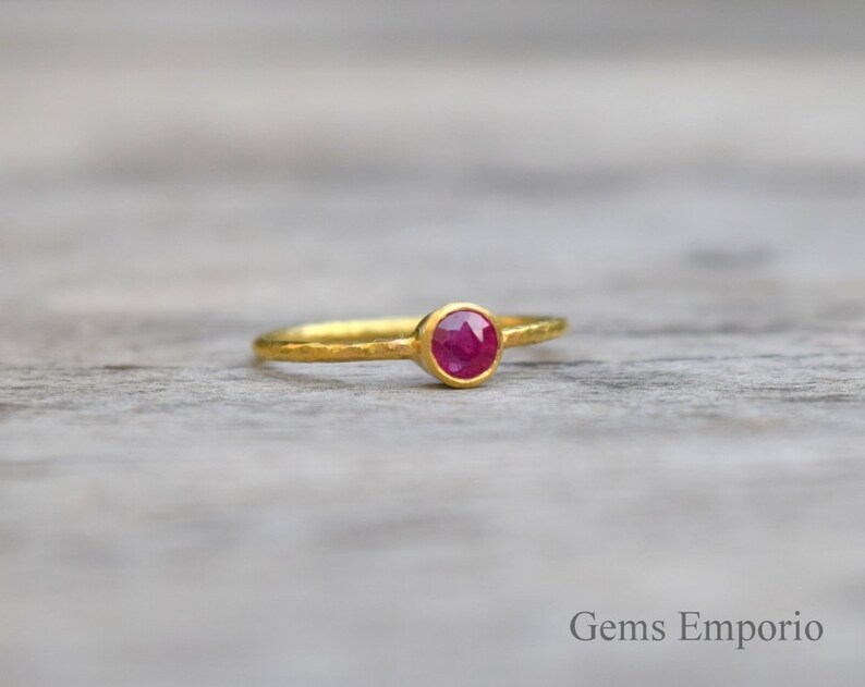 Pu&ograve; includere: Un anello d'oro con una pietra preziosa di rubino rosso. L'anello ha una texture martellata.