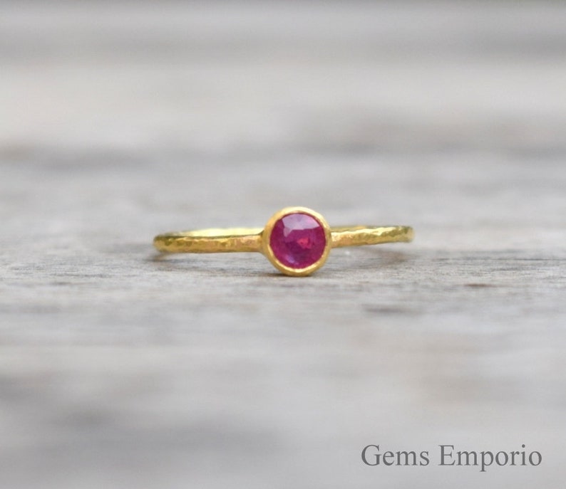 Pu&ograve; includere: Un delicato anello d'oro con una texture martellata e una piccola pietra di rubino rotonda.
