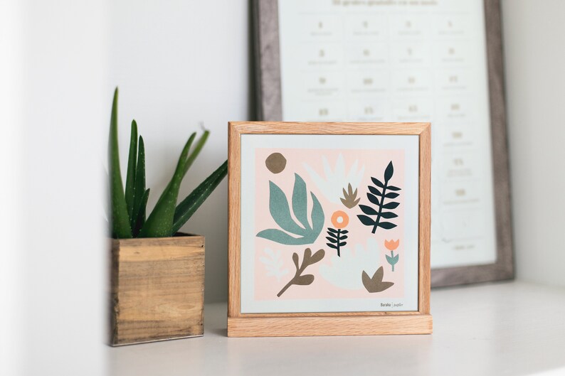 Puede incluir: Una impresi&oacute;n enmarcada con un fondo rosa y un dise&ntilde;o floral abstracto colorido. La impresi&oacute;n presenta hojas y flores verdes, azules, naranjas y marrones. El marco es de madera clara.