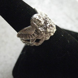 May include: A silver ring with a detailed design of two owls facing each other. The ring is on a black velvet display stand.
