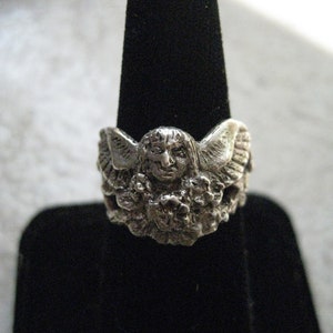 May include: Silver ring featuring a detailed sculpted angel with wings and a floral design.