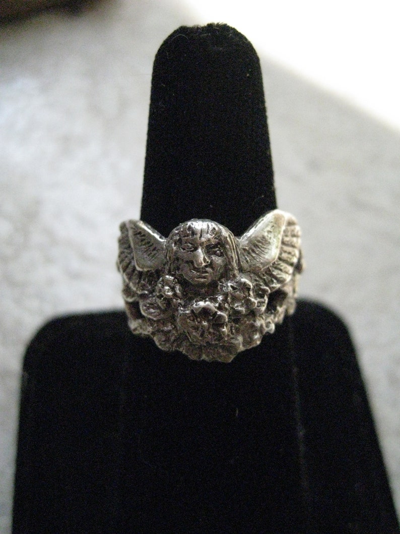 May include: Silver ring featuring a detailed sculpted angel with wings and a floral design.