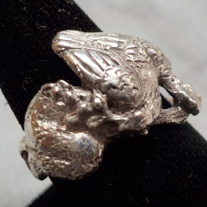 Op de afbeelding: Een zilveren ring met een gedetailleerd ontwerp van een vogel die een kleinere vogel in zijn klauwen draagt.