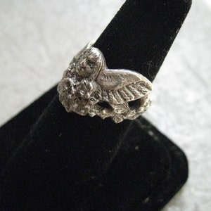 May include: A silver ring featuring a detailed sculpted owl design. The owl is perched on a branch with leaves and flowers.