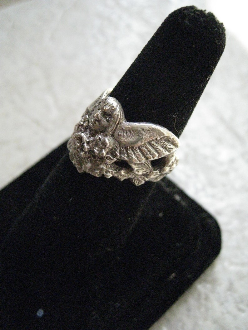 May include: A silver ring featuring a detailed sculpted owl design. The owl is perched on a branch with leaves and flowers.