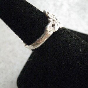 May include: A silver ring with a textured, organic design. The ring is displayed on a black velvet ring holder.
