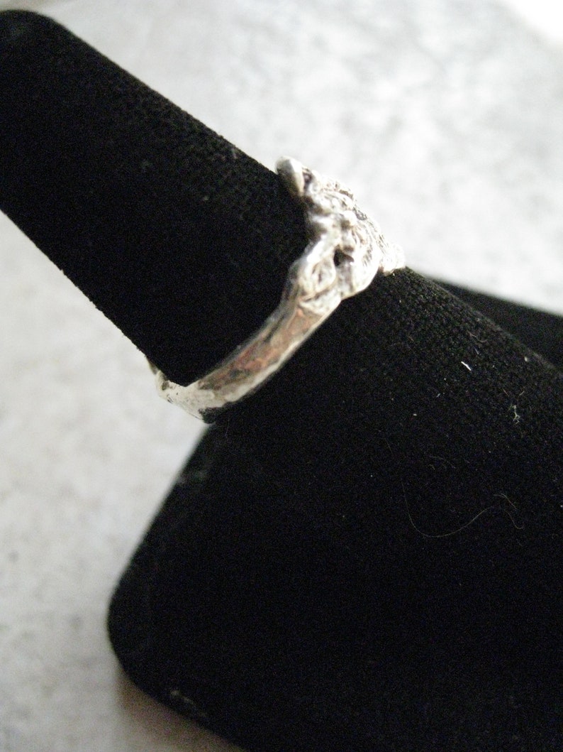 May include: A silver ring with a textured, organic design. The ring is displayed on a black velvet ring holder.