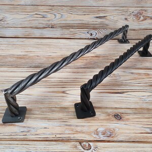 May include: Two black metal door handles with a twisted rope design. The handles are mounted on square plates.