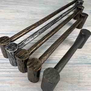 Könnte beinhalten: Ein Set aus fünf Metall-Schrankgriffen mit einer texturierten, rindenartigen Oberfläche. Die Griffe weisen verschiedene Metallic-Töne wie Bronze, Silber und Anthrazit auf, jeweils mit einer zylindrischen Stange und zwei stabilen Halterungen.