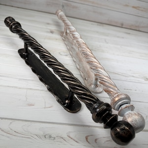 Könnte beinhalten: Zwei Türgriffe aus Metall mit gedrehtem Seildesign und kugelförmigen Endstücken. Ein Griff hat ein dunkelbronzenes Finish, der andere ein abgenutztes weiß-silbernes Finish. Beide Griffe sind auf länglichen Metallplatten mit gewelltem Rand montiert.