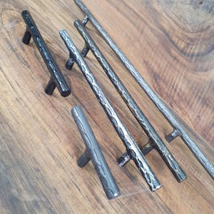 May include: Four black metal cabinet pulls with a hammered finish. The pulls are different sizes and have a T-shaped design.