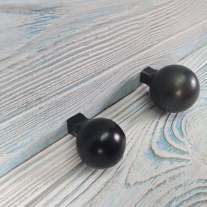 May include: Two black round cabinet knobs with a square base are mounted on a light blue and white wood surface.