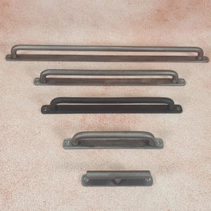 May include: Five different sizes of metal drawer pulls in various finishes, including black, silver, and brushed nickel. The pulls are all rectangular with rounded edges and a single, centered handle.