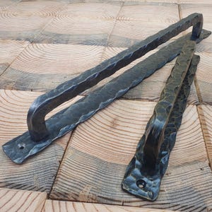 Peut inclure: Deux poignées en fer forgé noir, avec une finition martelée texturée. L'une est une longue tirette rectangulaire avec une poignée incurvée, l'autre est de conception similaire, mais plus petite. Les deux ont des plaques de montage.