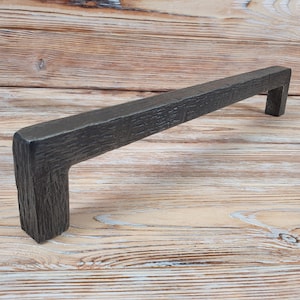 May include: A dark grey metal cabinet pull with a textured finish. The pull has a rectangular shape with rounded corners and a slight curve in the middle.