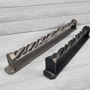 May include: Two black metal door handles with a twisted rope design. The handles are mounted on a black metal plate.