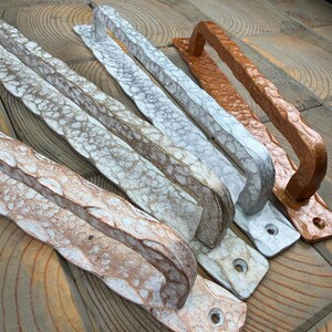 Könnte beinhalten: Drei Türgriffe aus Metall mit gehämmertem, strukturiertem Finish. Ein Griff ist kupferfarben, einer silberfarben mit weißer Patina und einer hellbronze mit weißer Lasur. Jeder Griff verfügt über Befestigungslöcher an den Enden.