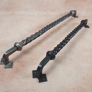 Op de afbeelding: Twee zwarte metalen deurgrepen met een gedraaid ontwerp. De grepen zijn ongeveer 30 cm lang en hebben een vierkante basis.