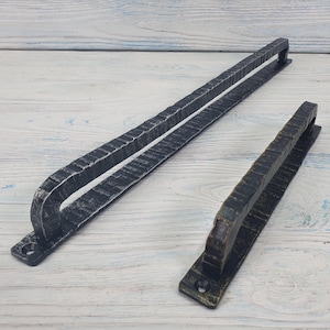 Può includere: Due maniglie per porte in ferro battuto. Una è lunga e rettangolare, l'altra è più corta. Entrambe hanno un aspetto strutturato e martellato e sono verniciate in tonalità di nero e bronzo. Le maniglie sono progettate per essere montate su una porta.