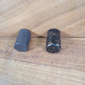 May include: Two black cylindrical knobs with a slightly distressed finish. The knobs are made of metal and have a slightly rounded top.