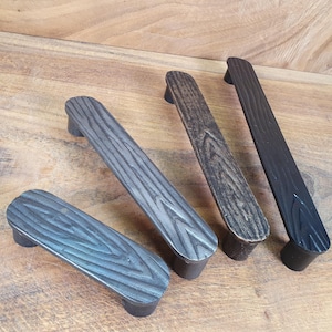 May include: Four black metal cabinet pulls with a wood grain texture. The pulls are in different sizes and are arranged in a row.