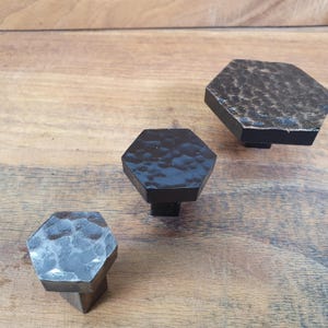 May include: Three black hexagonal cabinet knobs with a hammered finish. The knobs are of different sizes.