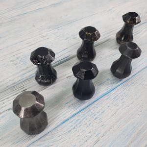 May include: Six black and silver decorative knobs with a faceted design. The knobs are arranged in two rows on a light blue wooden surface.