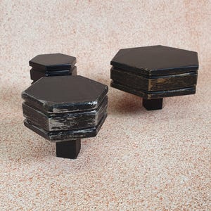 Puede incluir: Tres soportes de madera hexagonales negros de diferentes tamaños. Los soportes tienen un acabado desgastado y son perfectos para exhibir objetos pequeños.